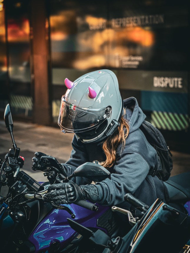 Motorcyclist riding with custom helmet featuring small pink horn accessories by Helmet Flair