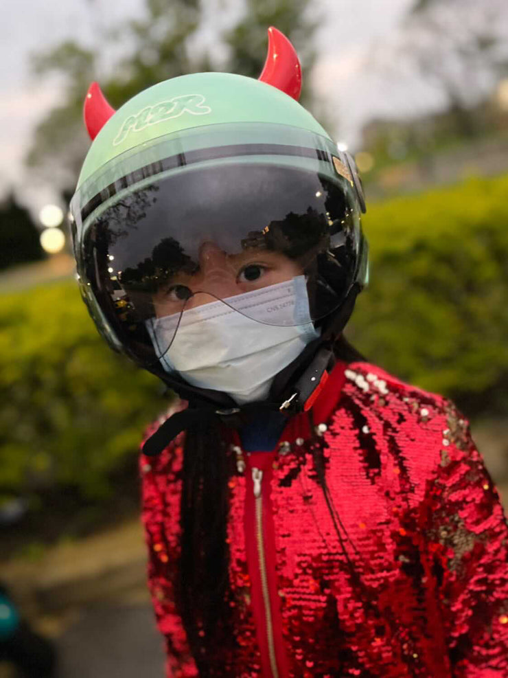 Child with small red devil horns on a motorcycle helmet