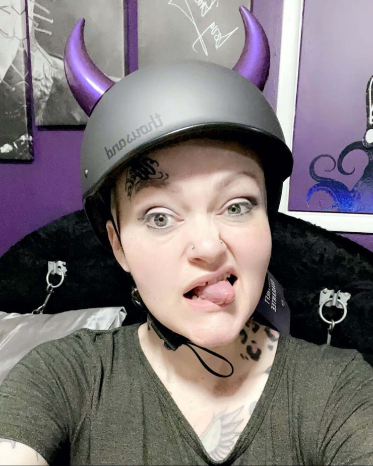 Large purple horns on a skate helmet worn by a woman sticking her tongue out