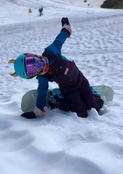 Child with a snowboard with small gold horns on his snowboard helmet
