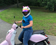 Pink cat ears on a scooter helmet worn by a woman riding a pink scooter