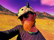 Small black horns on a bicycle helmet worn by a man with a red beard with the mountains in the background